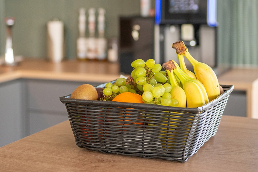 Obstkorb im Aufenthaltsraum mit Bananen, Trauben, Äpfeln, Kiwis und Orangen